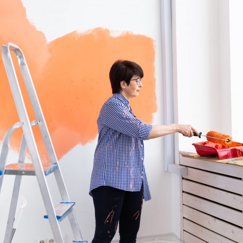 Renovation, redecoration and repair concept - middle-aged woman painting wall in new apartment.